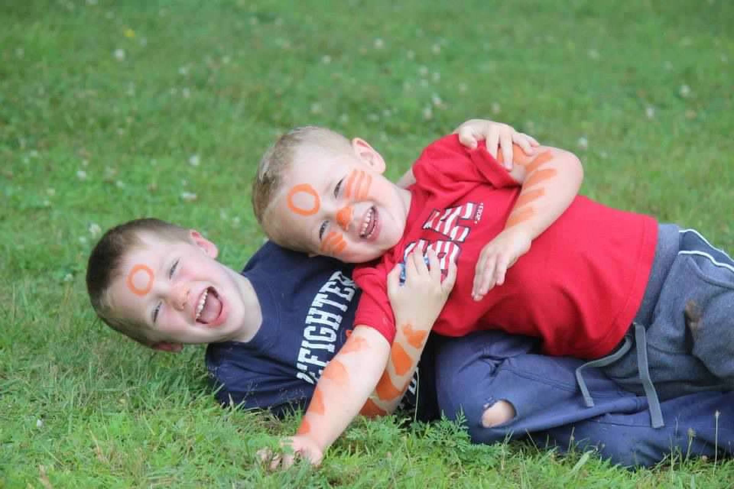 Two young boys with orange face paint, laughing in the grass at camp