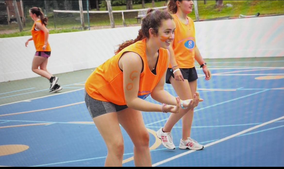 Jori Horn in an orange Susquehannock pinnie with orange face paint, ready on the camp sport court