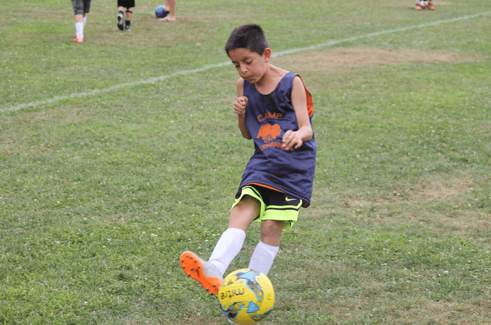 A young Manny Pinzón dribbling a soccer ball on the field at camp